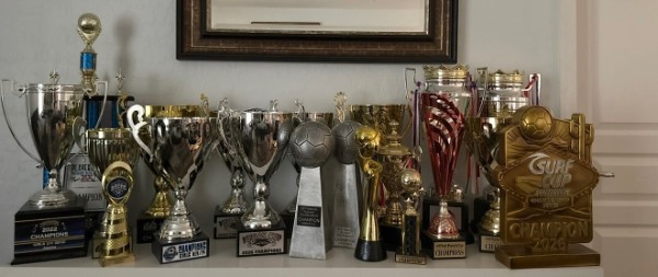 Shelf of Storm FC championship trophies, including the Surf Cup 2026 champion trophy
